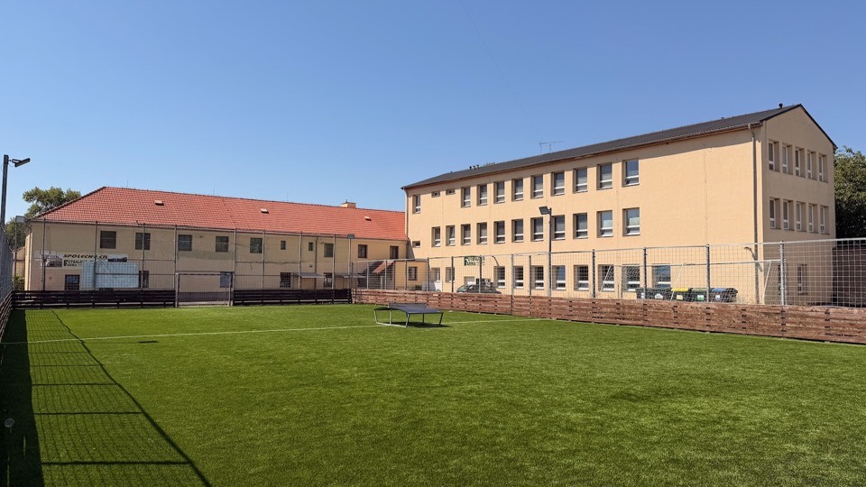 Venkovní hřiště s umělým trávníkem ve dvoře areálu, v pozadí obě budovy ubytovny Vědomice
